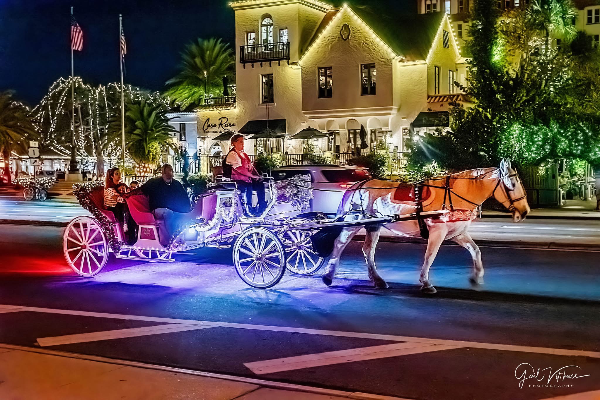 A horse-drawn carriage carrying guests past illuminated buildings in St. Augustine.